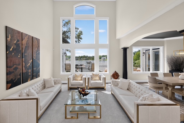 The two-storey great room with tufted sofas and a wall of windows framing the lake