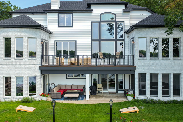 Elevated view of the estate's rear elevation with upper deck seating, covered lower patio and lawn