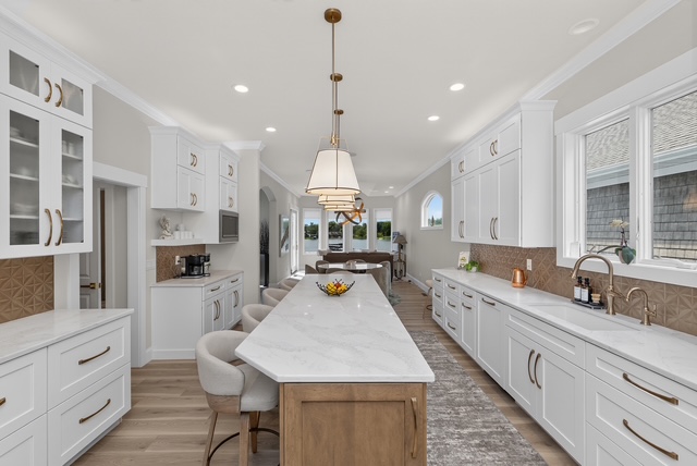 The chef's kitchen with a long marble island, oak base, brass pendants and white cabinetry